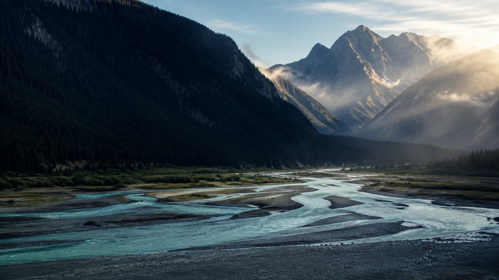 A wide alpine valley with forested mountains and rivers coming together